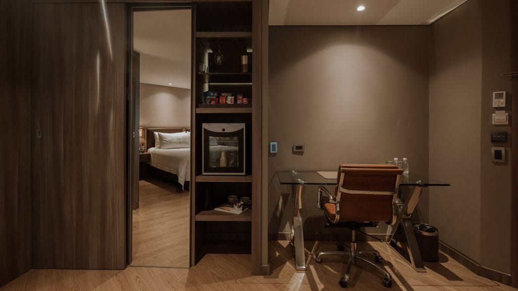 Junior Suite Deluxe en Binn Hotel Medellín con escritorio moderno, minibar integrado y vista a dormitorio elegante con iluminación cálida