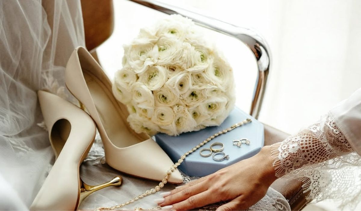 Accesorios de novia con ramo blanco, zapatos de tacón y joyería sobre una silla.