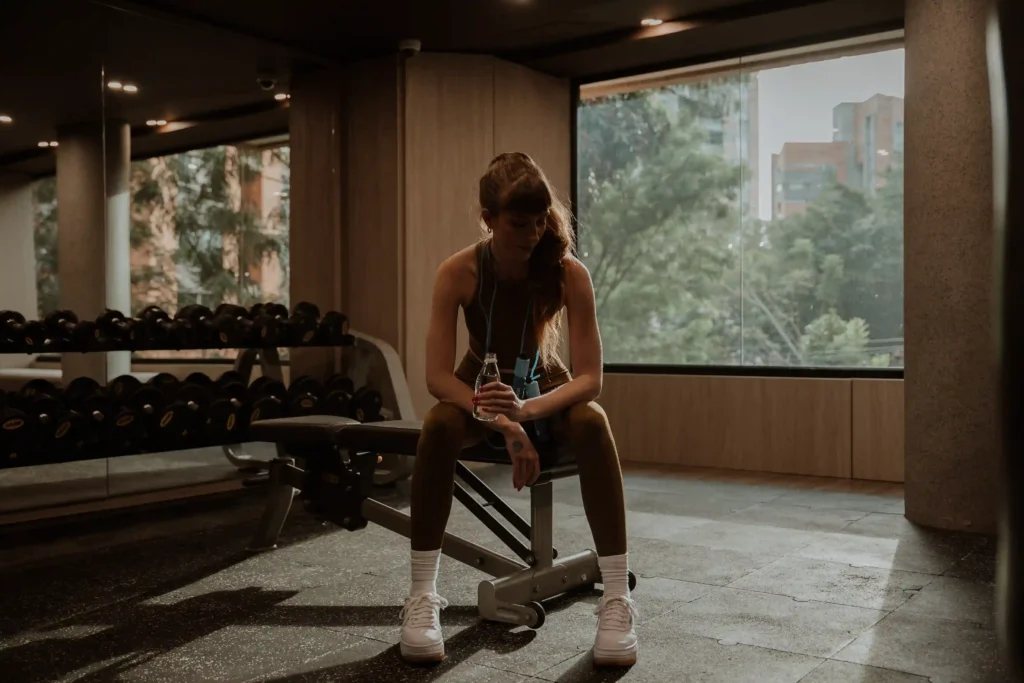 Mujer descansando en banco del gimnasio de BINN Hotel con mancuernas al fondo.