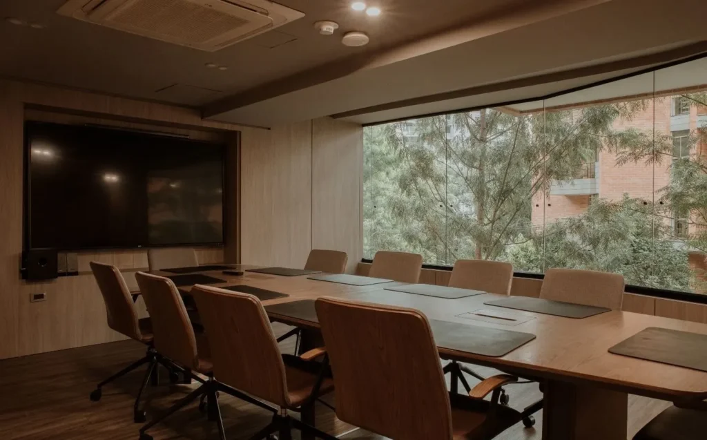 Sala de reuniones de BINN Hotel con mesa larga, pantalla y vista a árboles.