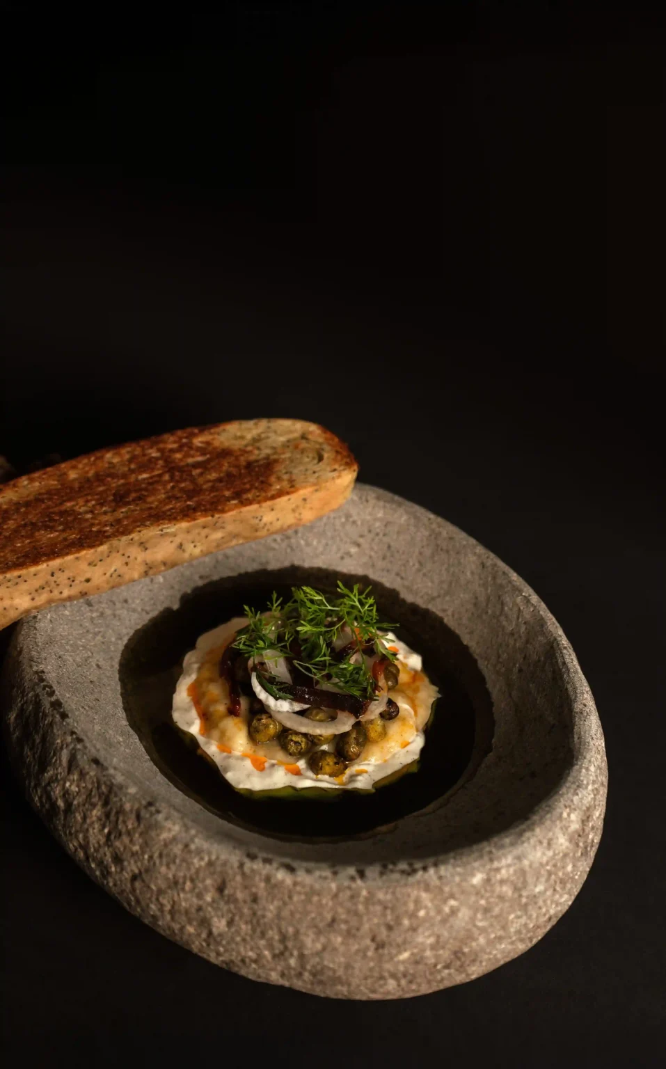 Gourmet Colombian cuisine dish served in a stone bowl with cream, garnishes, and toasted bread.