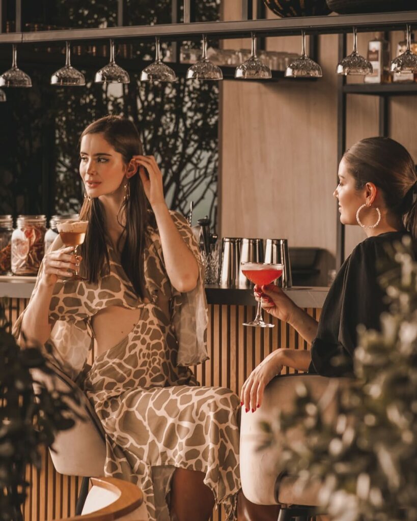 Dos mujeres sentadas en una barra, disfrutando de sus bebidas y cena gourmet