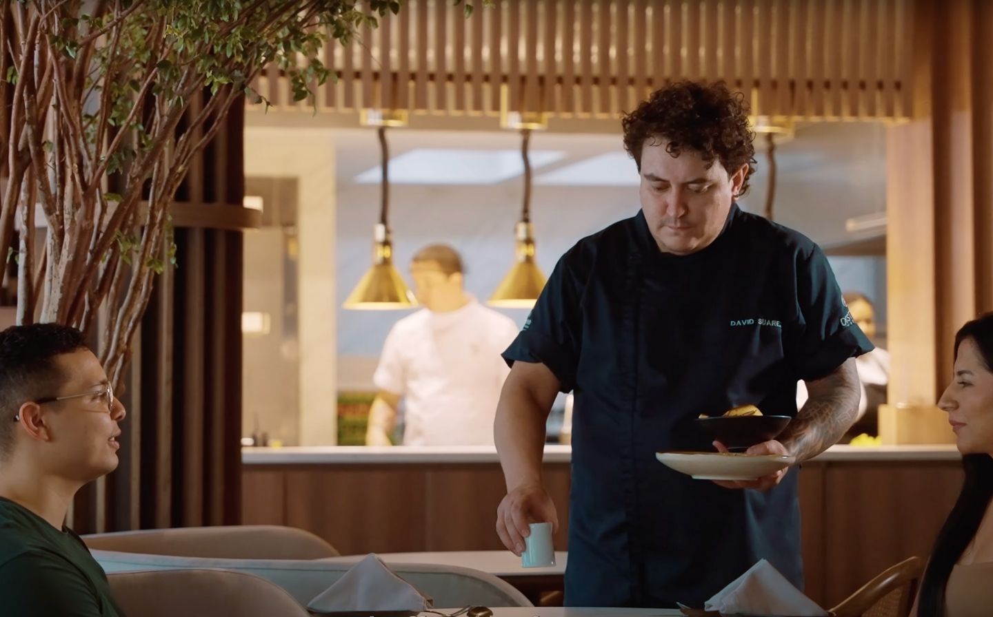 El chef david suarez estrada sirviendo comida a dos personas en un restaurante acogedor