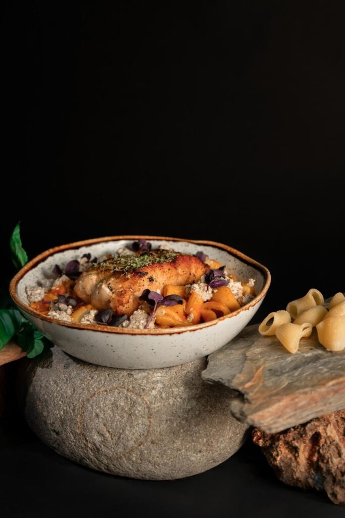 Un tazón de pasta con pescado sobre una piedra, decorado con hierbas frescas y un toque de aceite de oliva, mostrando una presentación: arte en el plato.