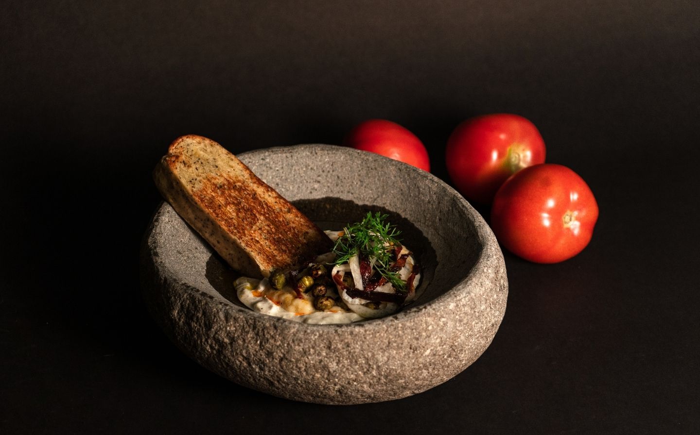 Un cuenco de piedra con pan y tomates frescos sobre una mesa, parte del menú degustación de 7 pasos en La Makha.