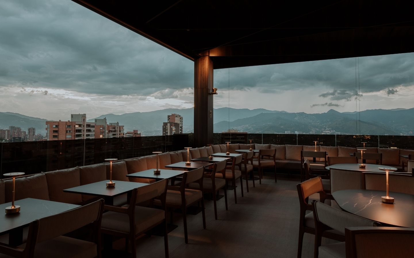 Rooftop exclusivo en Medellín con vistas a las montañas. El restaurante tiene un ambiente acogedor y natural con mesas y sillas de madera.