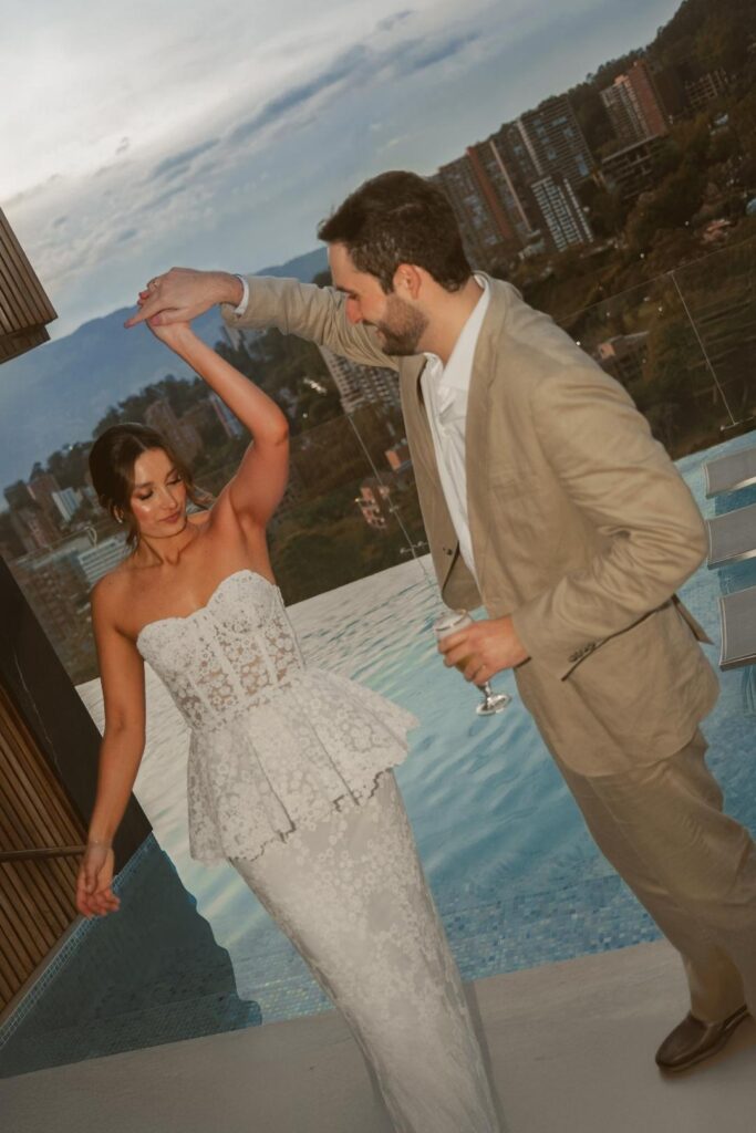 A couple dances on a balcony, celebrating their wedding with a breathtaking city view behind them.