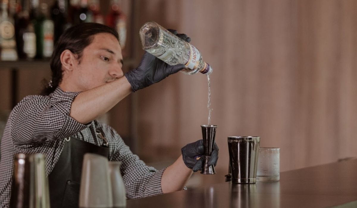 Un bartender sirviendo una bebida en un vaso, mostrando habilidad en un entorno de bar animado.