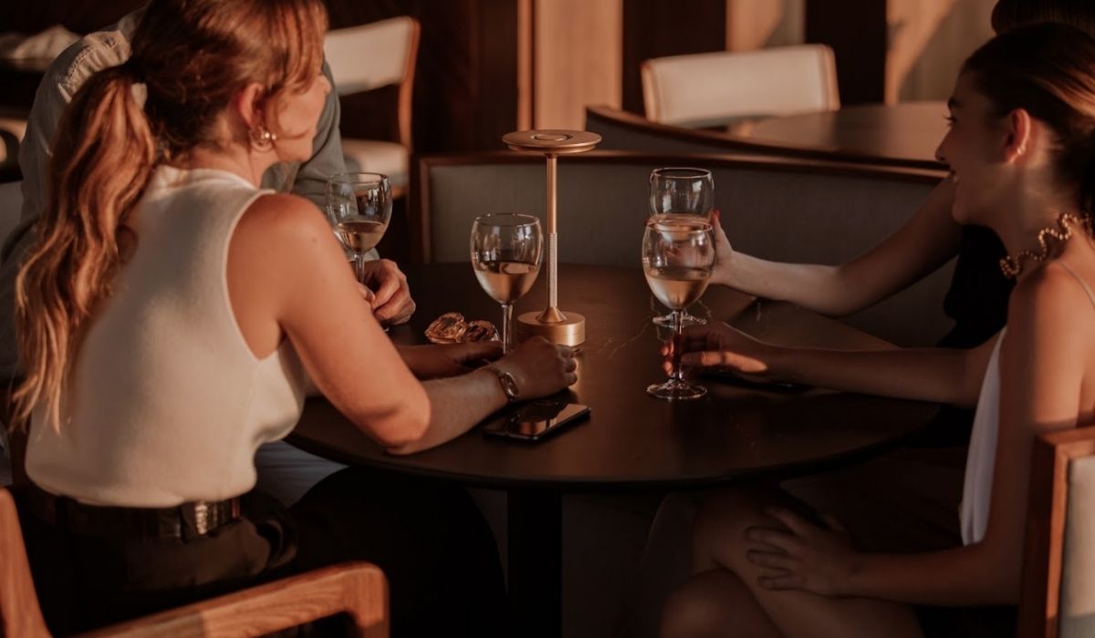 Three women at a table, with glasses of wine, sharing laughter and pleasant moments.