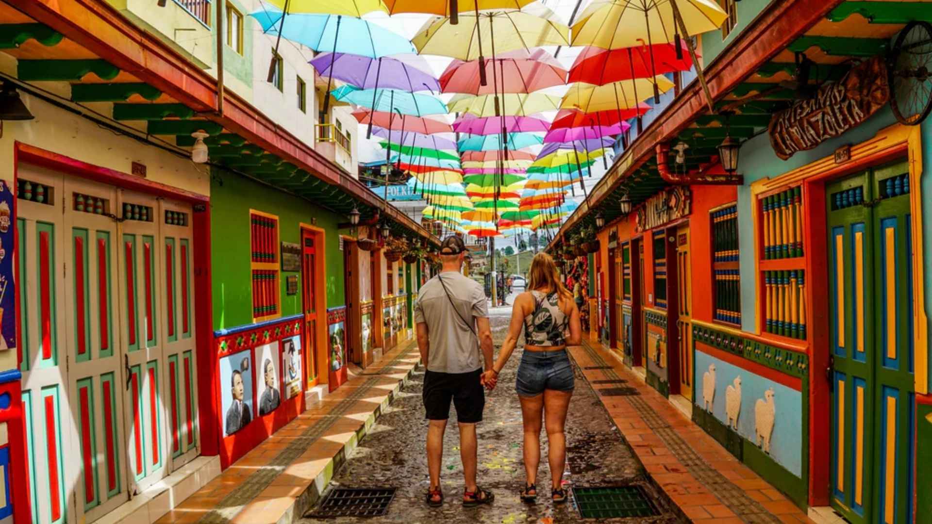 Pareja de la mano caminando por un colorido callejón con paraguas, en un destino premium cerca de Medellín
