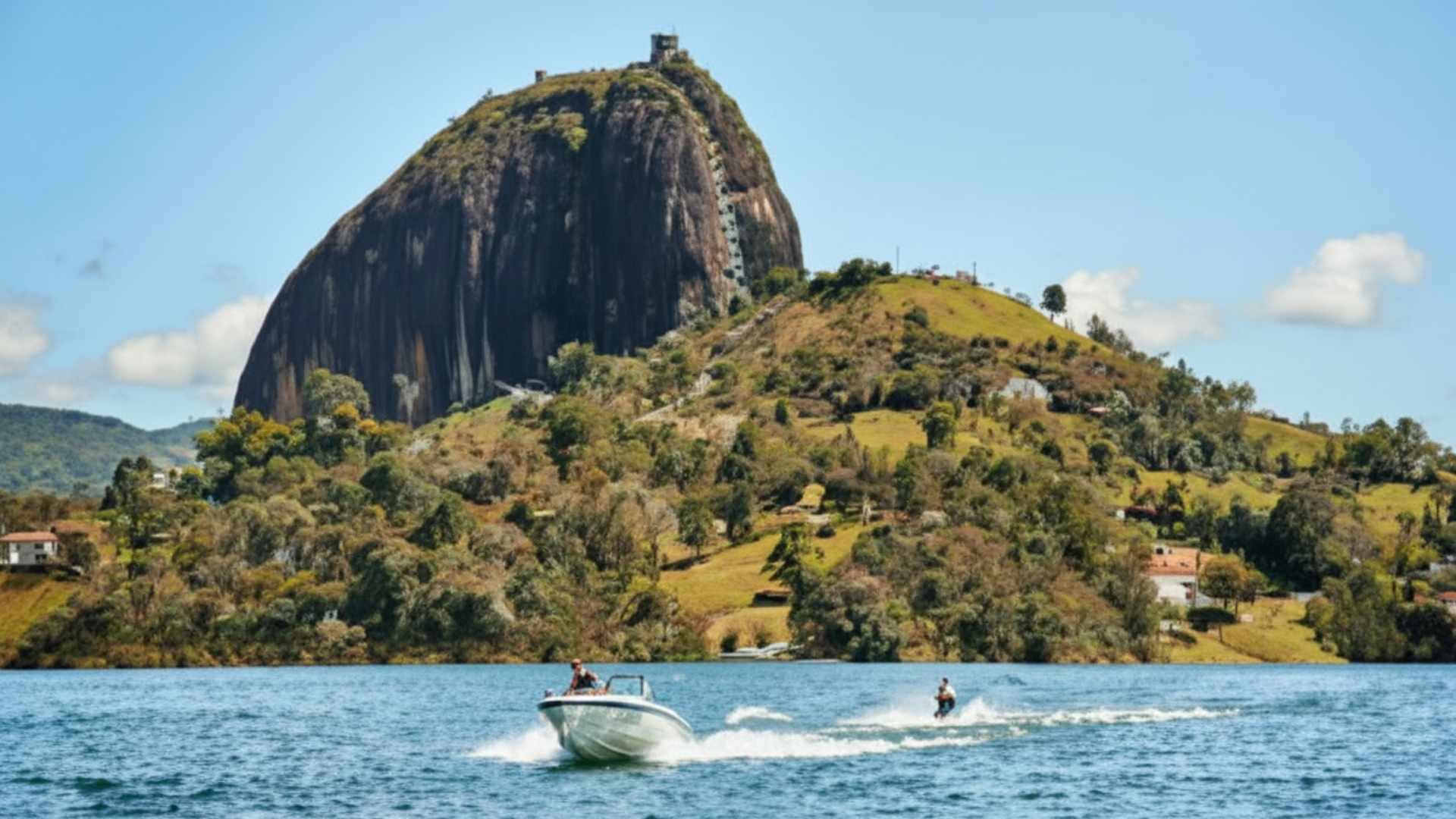 A boat sails through the water near a mountain in Guatapé, showing a beautiful landscape near Medellín.
