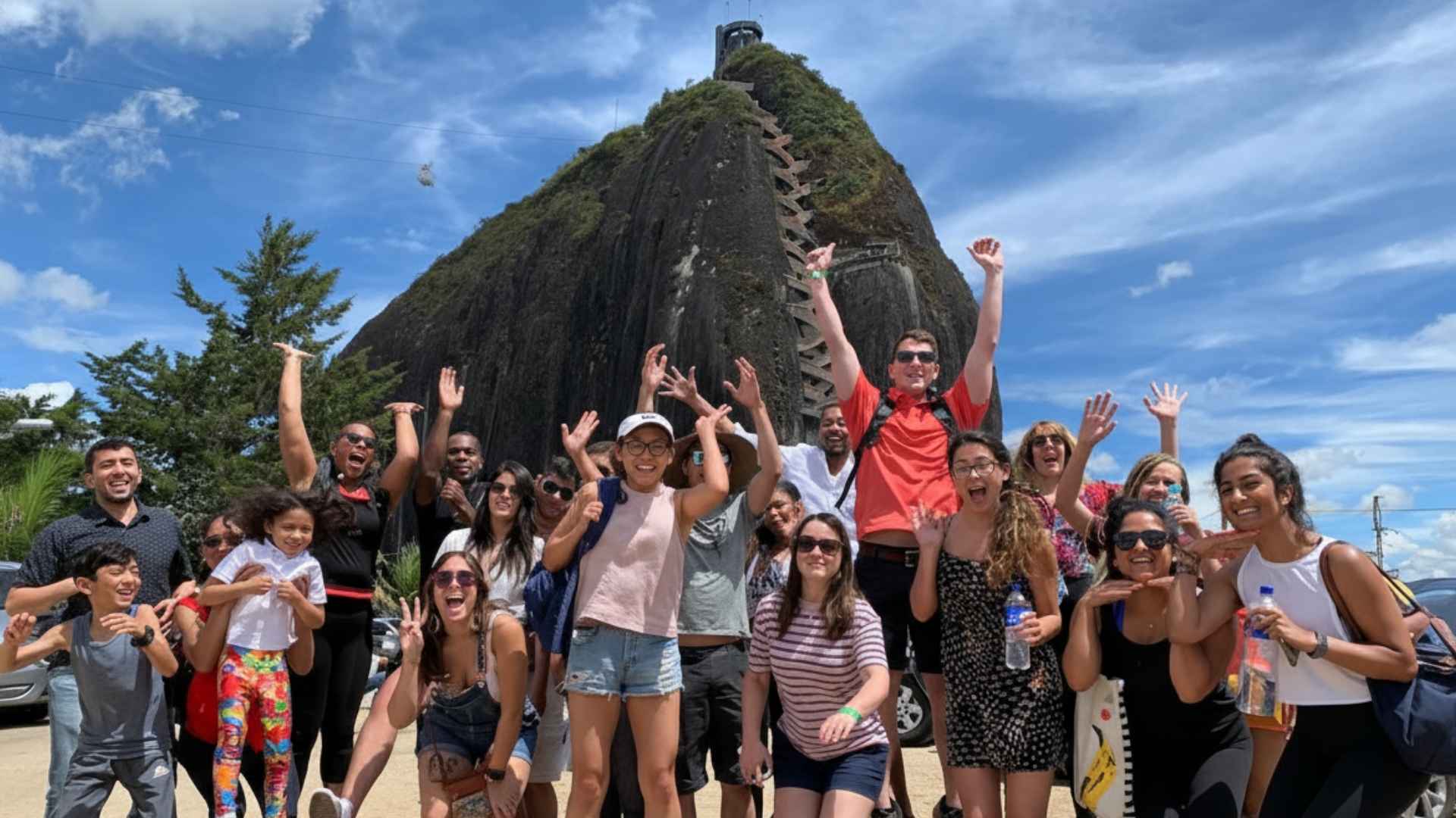 Grupo de personas sonriendo frente a una majestuosa montaña guatape en Antioquia, disfrutando de una experiencia de lujo