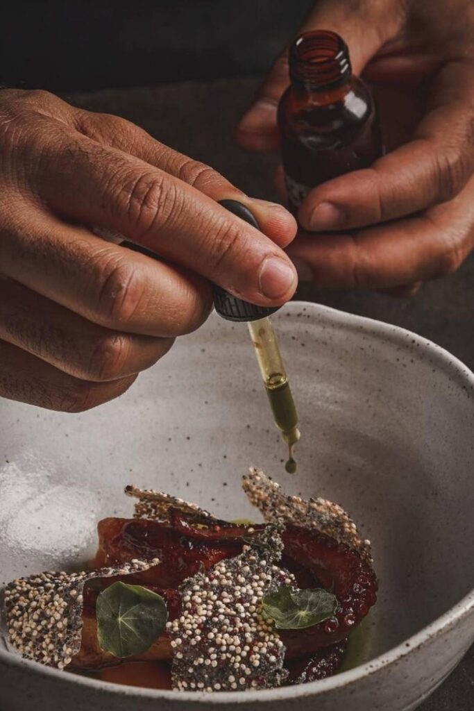 Un hombre vierte aceite sobre un plato de comida en el contexto de Fusión o identidad en La Makha