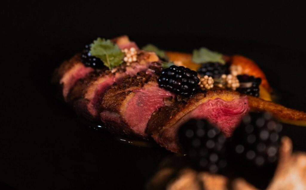 Un plato negro con carne, moras y nueces, representando la fusión de arte local y gastronomía en La Makha