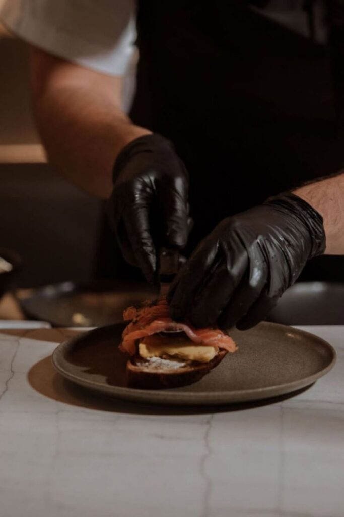 Chef wearing black gloves preparing a sandwich at La Makha, fusing local fishing with haute cuisine
