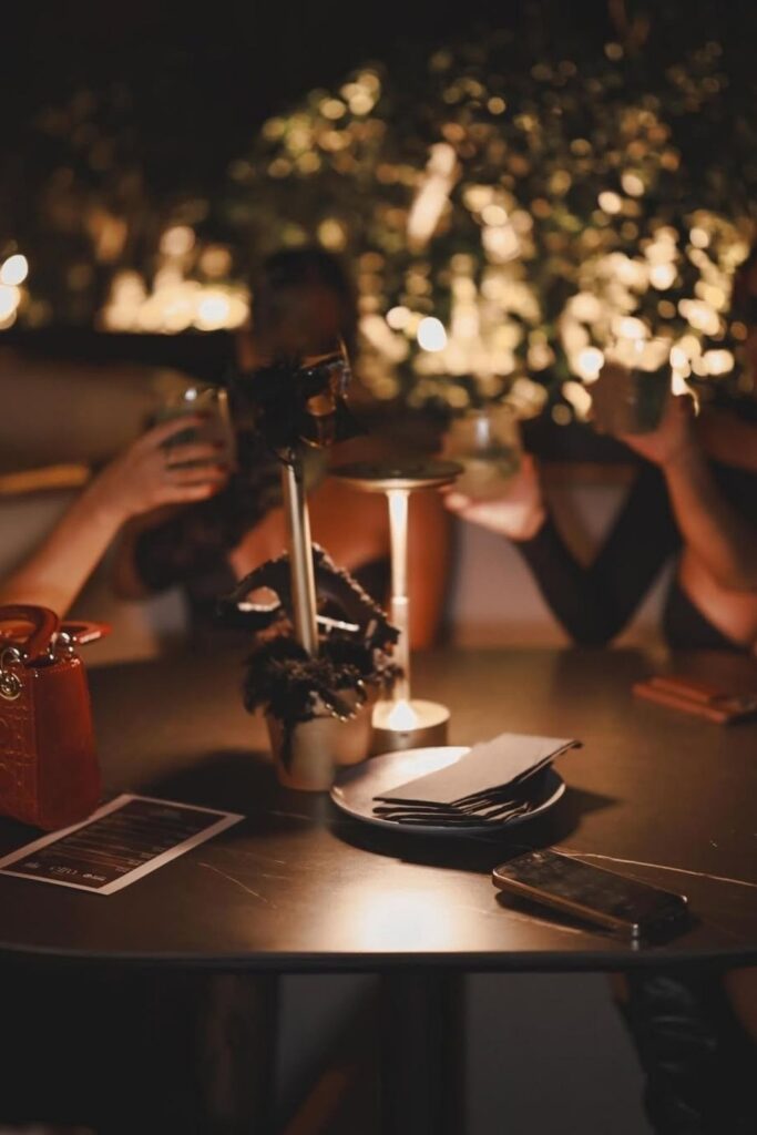 Personas compartiendo risas y bebidas en una mesa, en un ambiente nocturno y acogedor de diseño íntimo de Etro