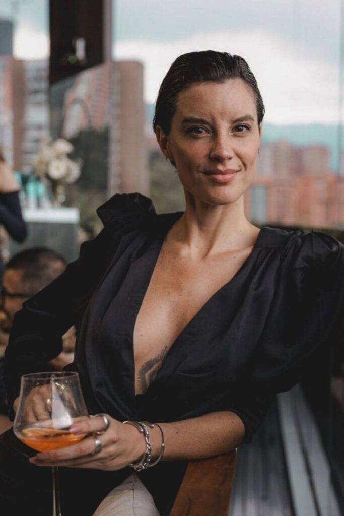 Mujer tatuada en vestido negro sosteniendo una copa de vino en un evento corporativo de lujo en Medellín