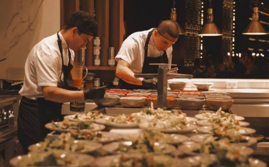 Dos hombres con delantales blancos preparando comida en un restaurante, reflejando la elegancia de eventos en el BINN Hotel
