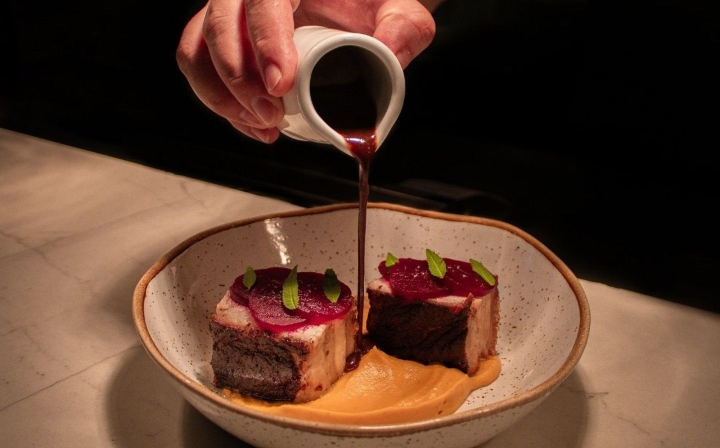 Persona vertiendo salsa sobre un plato de carne, destacando la narrativa visual de la makha
