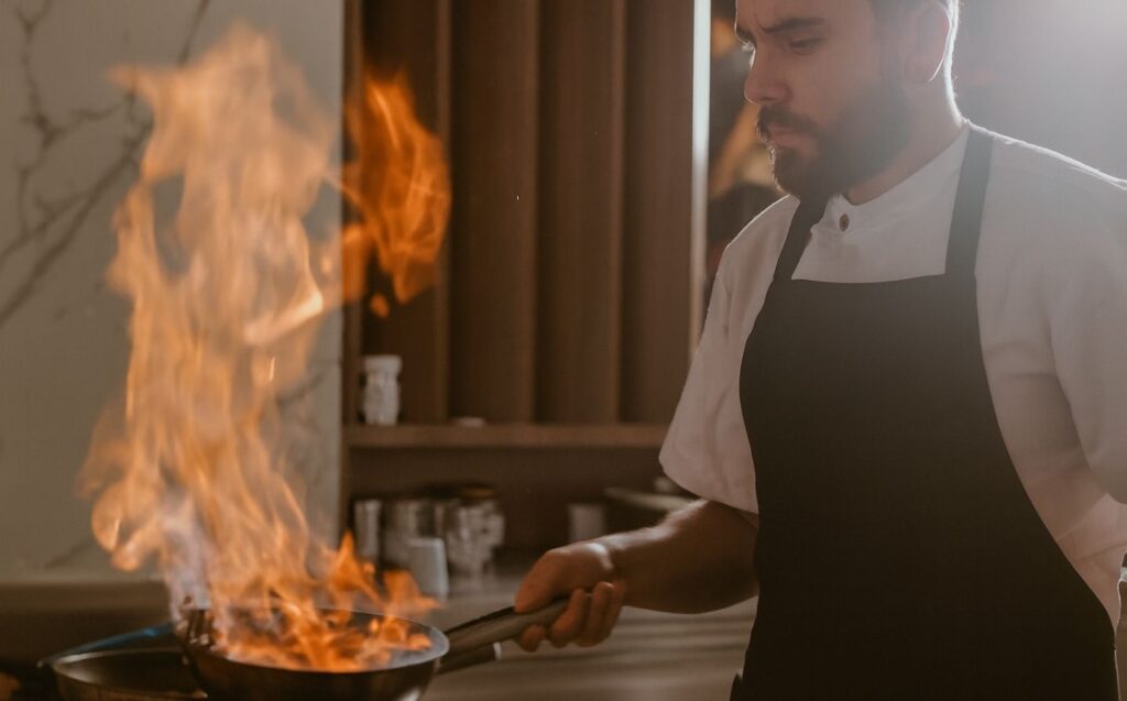 Hombre con delantal de chef cocinando en la estufa, preparando platos perfectos para compartir en Etro