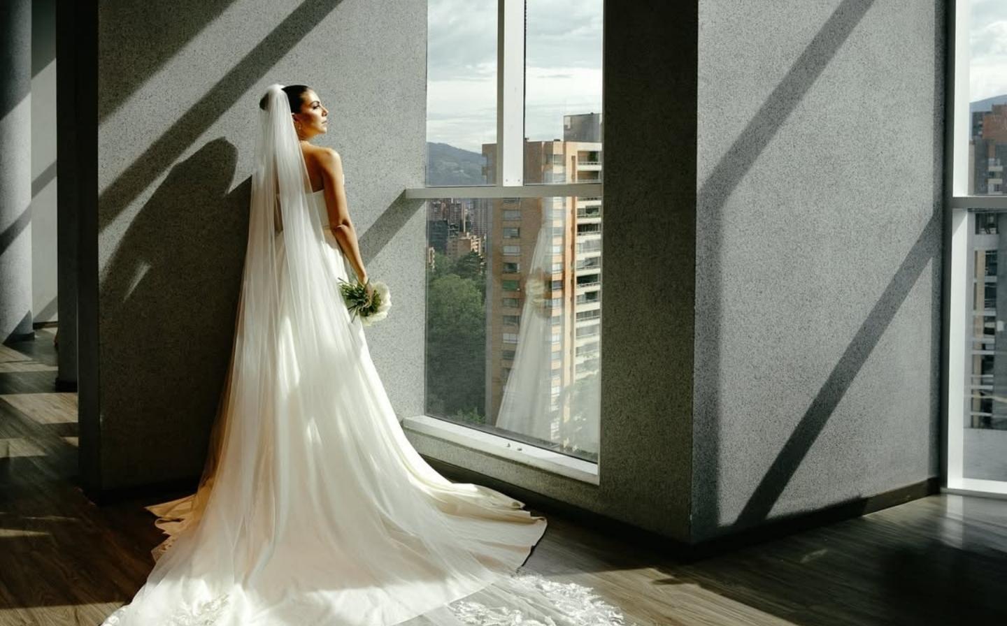 A bride stands by a window, gazing at a stunning city view, showcasing the ideal hotel for your wedding