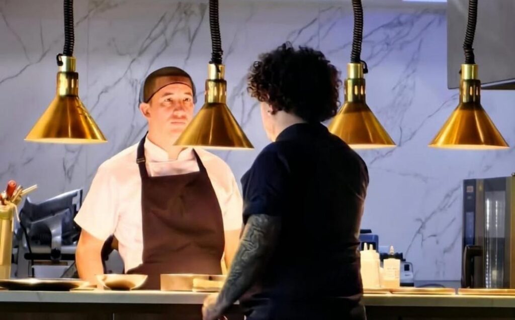 Dos chefs, David Suárez Estrada y su compañero, están de pie en un mostrador de restaurante, listos para cocinar