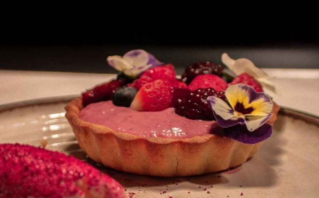 Postre decorado con frutas del bosque y flores, servido en un plato. Vive la experiencia completa de La Makha.