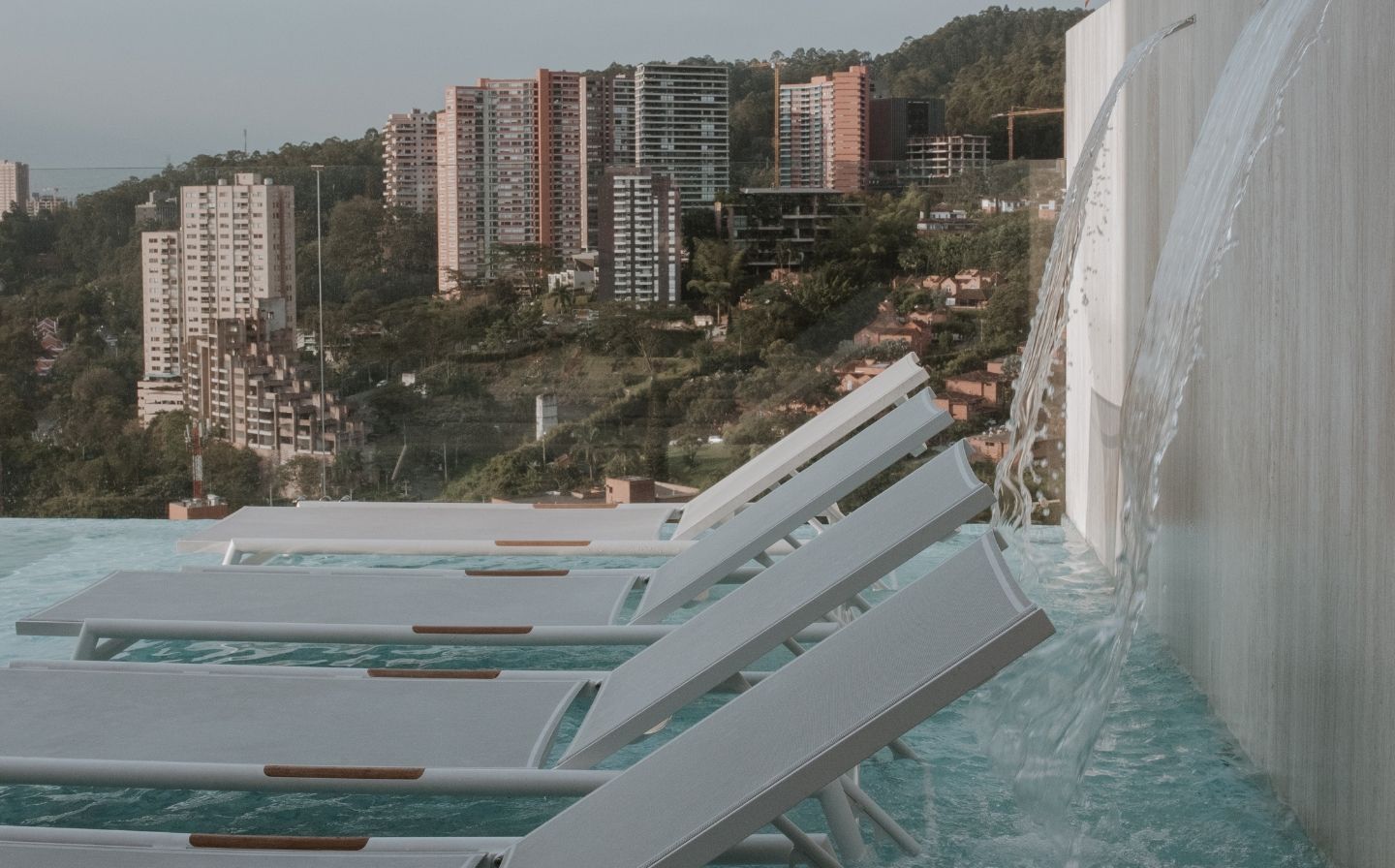 Lounge chairs by a pool offer a serene view of the city skyline, perfect for relaxation and wellness