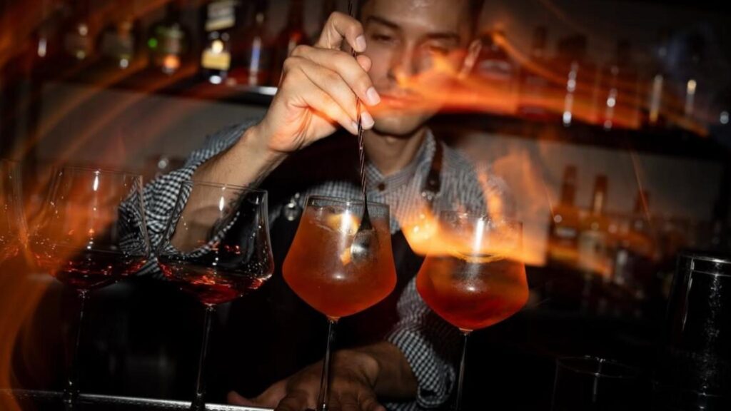 Un bartender vierte una bebida en llamas, mostrando su habilidad en el arte de la coctelería.