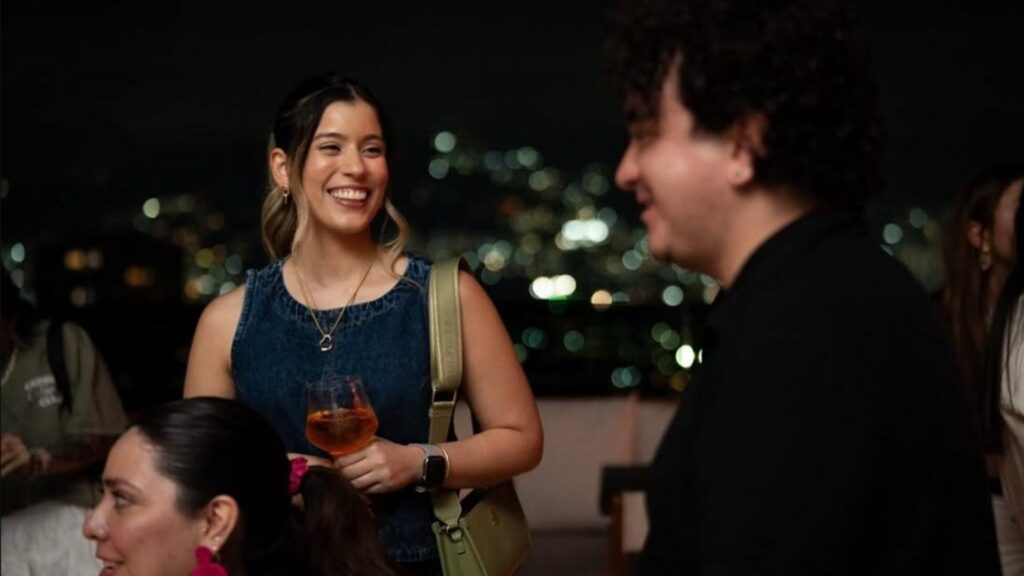 Un grupo de personas disfruta de bebidas en la azotea de Etro, iluminados por luces nocturnas.