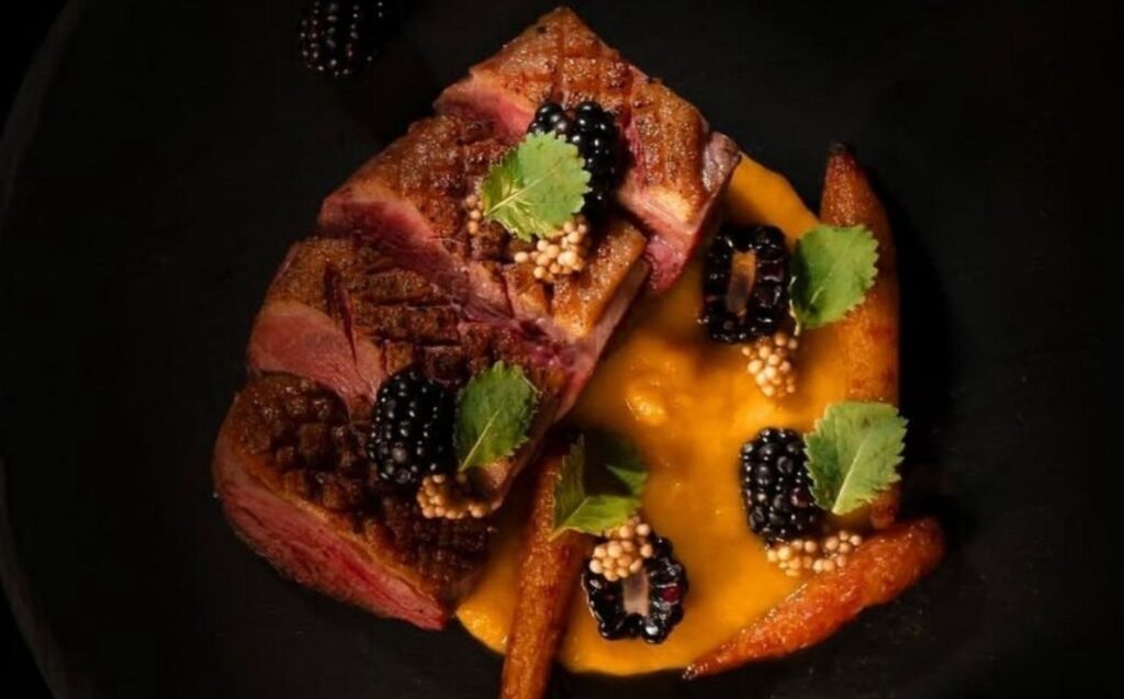 Un plato de carne jugosa acompañado de moras frescas.