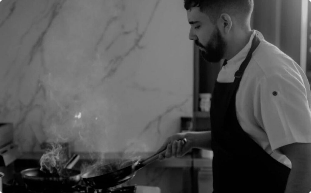 Chef cocinando en una cocina, con humo saliendo de la sartén