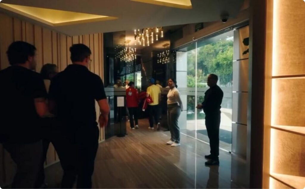 Personas de pie en un pasillo elegante, iluminado por un hermoso candelabro.