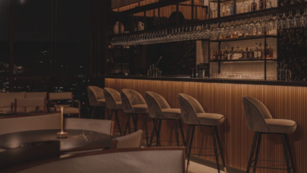 Un bar con sillas y una mesa frente a una ventana iluminada.