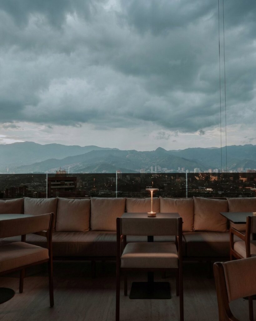 Terraza de rooftop al aire libre en Medellín con vista a montañas, mobiliario elegante y ambiente tranquilo con iluminación cálida