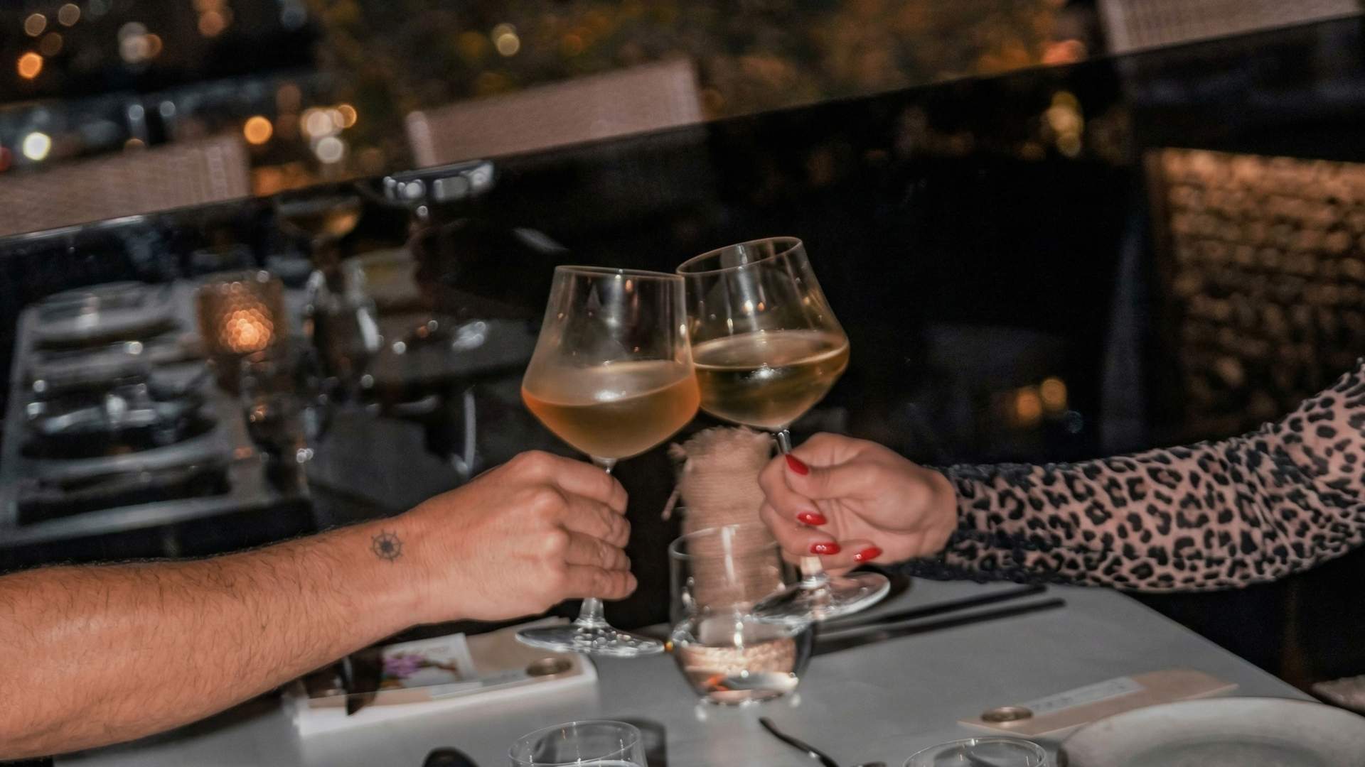 Pareja brindando con vino en rooftop romántico en Medellín, ambiente nocturno elegante con luces cálidas y vista urbana