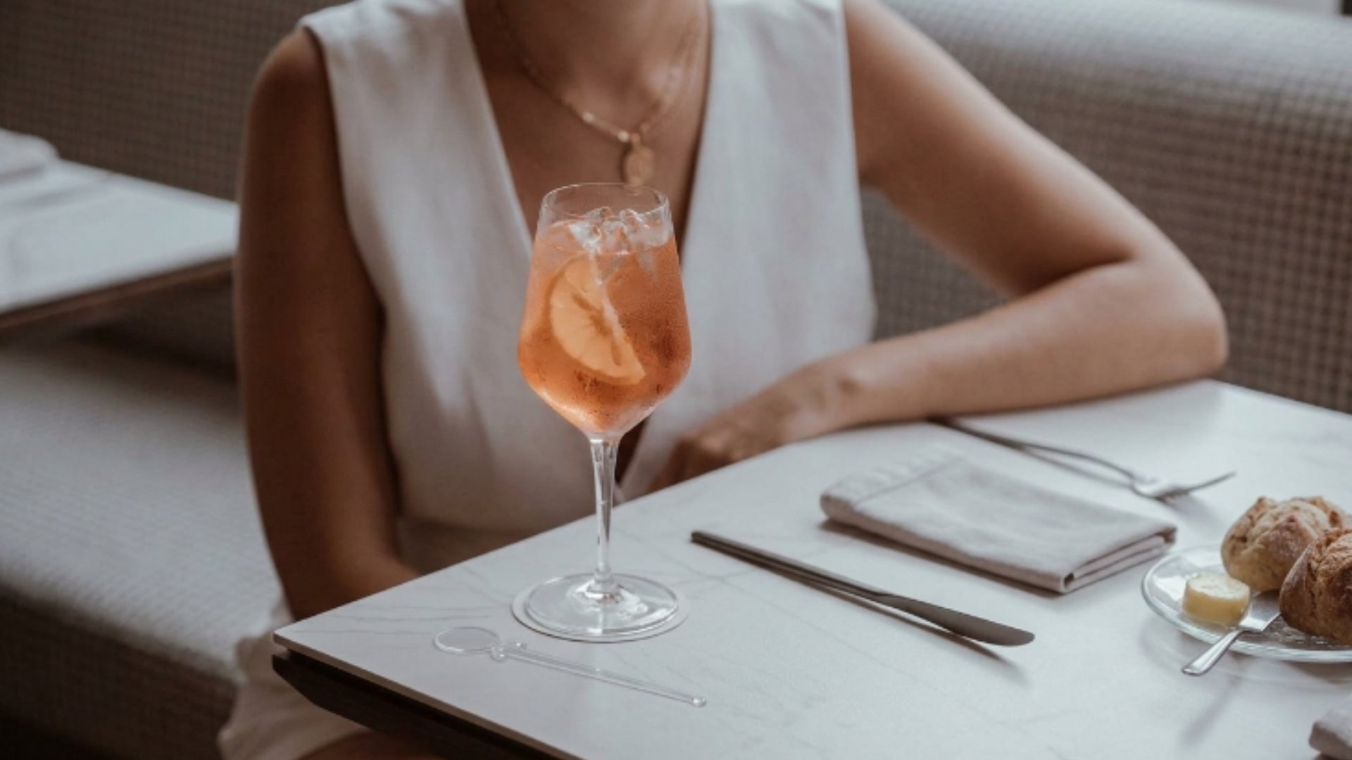 Cóctel artesanal con rodaja de naranja en rooftop de Medellín, ambiente elegante con mesa minimalista y experiencia premium de coctelería.