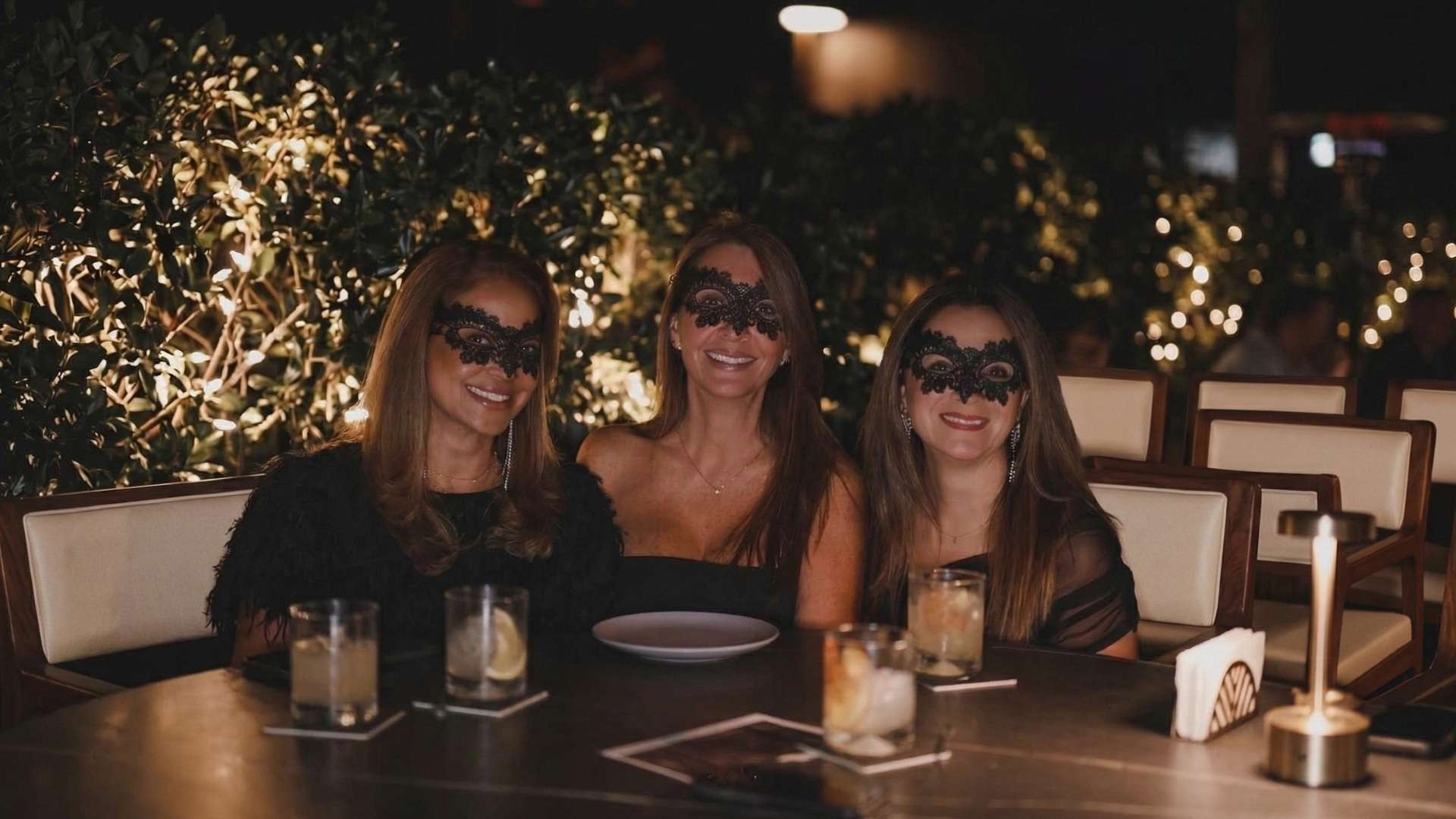 Grupo de amigas con máscaras brindando en rooftops en Medellín para salir hasta tarde, ambiente nocturno elegante con iluminación cálida.