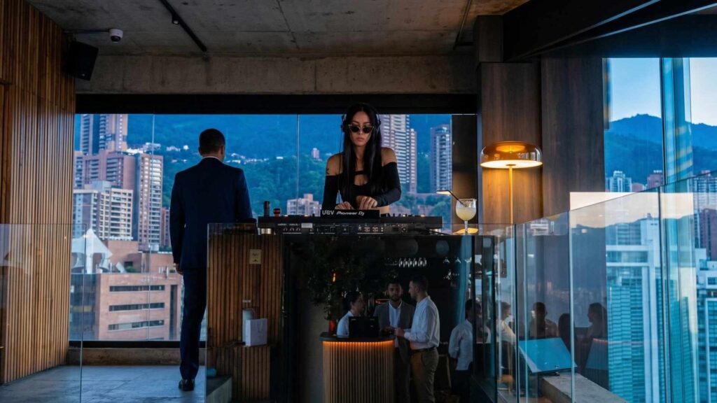 DJ tocando en rooftop con buena música en Medellín, vista urbana panorámica y ambiente moderno con personas socializando.