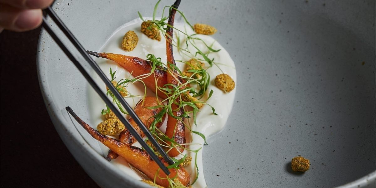 Plato de alta cocina en el restaurante La Makha de Medellín: zanahorias baby asadas sobre crema blanca y brotes.