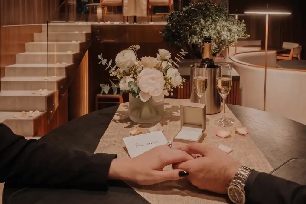 Propuesta de matrimonio exitosa en Etro Rooftop: manos entrelazadas con anillo de compromiso, champagne y flores.