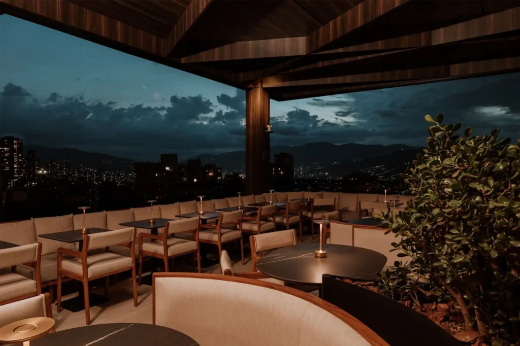 Rooftop bar moderno en Medellín al atardecer, con mobiliario elegante y vista panorámica desde una terraza cubierta.