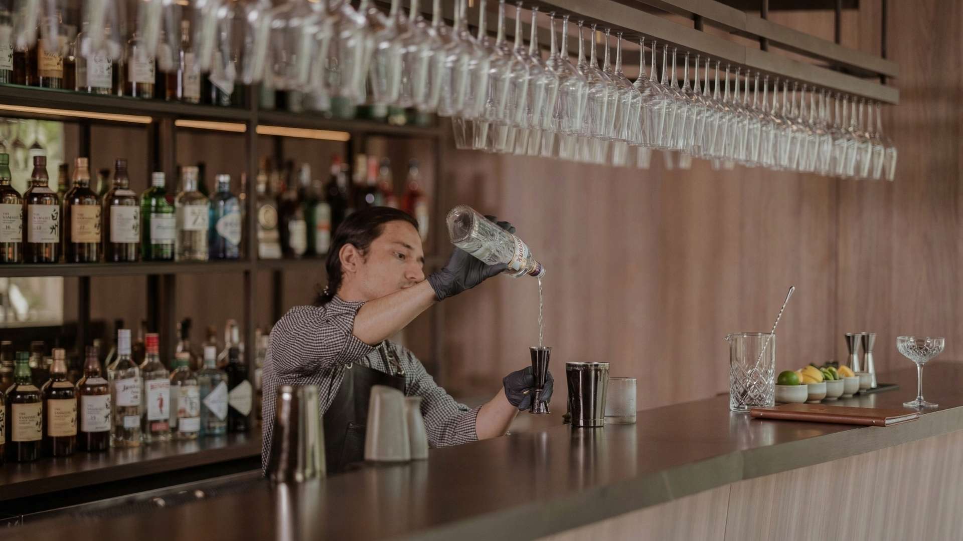Bartender profesional preparando cóctel en Etro Rooftop Medellín con barra elegante, botellas premium y cristalería suspendida