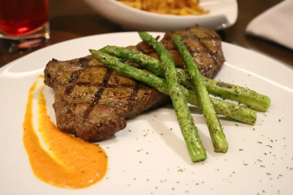 Corte de carne premium a la parrilla en restaurante La Makha Medellín: servido con espárragos trigueros y salsa artesanal.