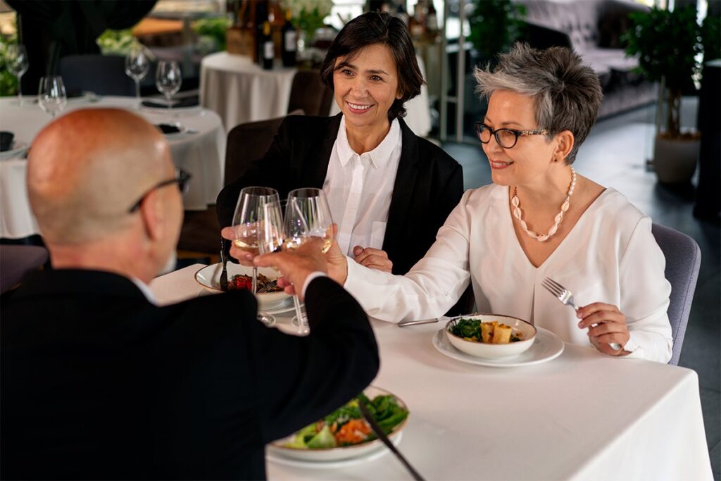 Tres personas mayores brindando con vino blanco en una cena formal en La Makha Restaurante
