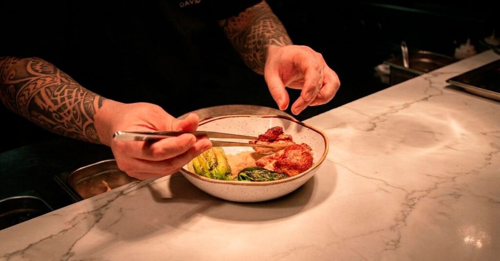 Chef David Suárez Estrada preparando y emplatando un plato gourmet con precisión en una cocina profesional