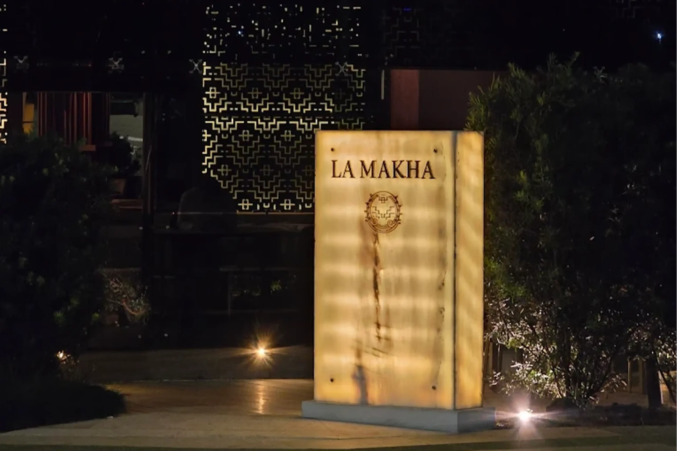 Entrada al restaurante La Makha en Medellín: tótem de mármol retroiluminado con logo dorado en un ambiente nocturno elegante.