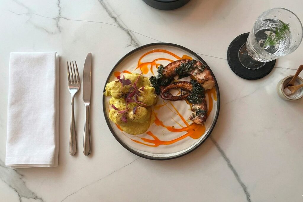 Plato de cocina fusión mediterránea y colombiana en La Makha Medellín: Pulpo grillado con papas criollas en salsa de cúrcuma sobre mesa de mármol.