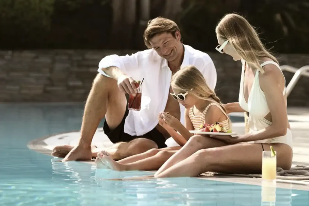 Vacaciones en Binn Hotel de lujo familiar en Medellín: padres e hija relajándose con snacks en zona de piscina premium.