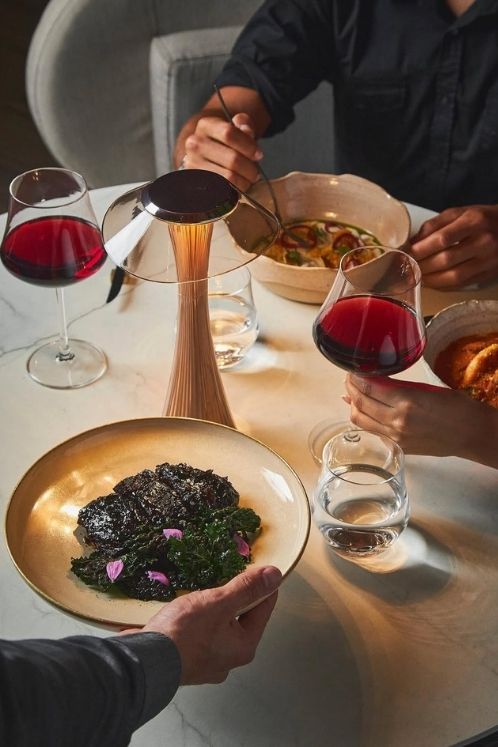 Cena para nómadas digitales en La Makha Medellín: platos de alta cocina, copas de vino tinto e iluminación cálida en un ambiente de lujo.